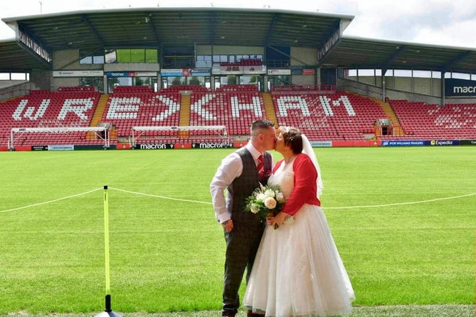 Debbie Roberts and Chris Roberts take photos at Wrexham's Racecourse Stadium on their wedding day.See SWNS story SWFTwrexham. A couple who bonded over their love of football tied the knot with a Wrexham AFC inspired wedding. Debbie Roberts, 39, got chatting to Chris Roberts, 36, in May 2022 on a dating app. They bonded over their mutual support of Wrexham FC