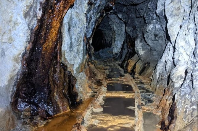 A disused track disappears into the black of a mine and its fading history